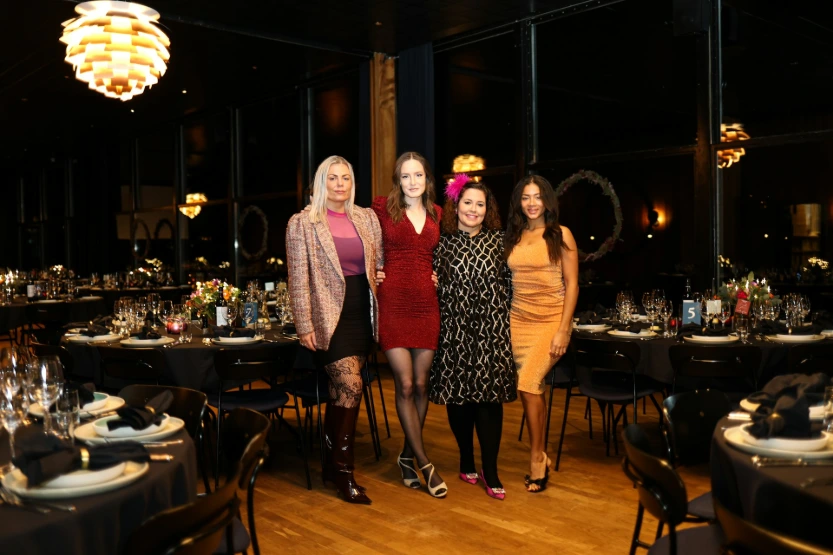 Four women posing in a formal dining room setting.